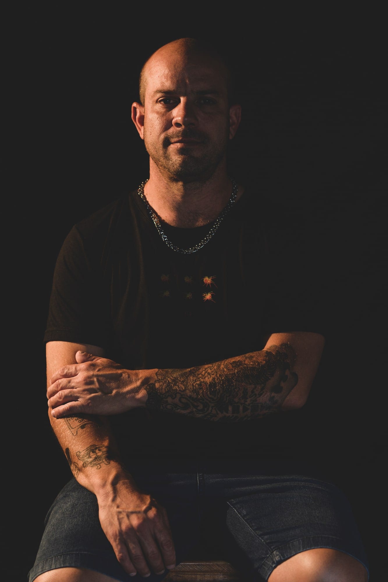 Studio portrait of Tomás Tassara seated against a black background, arms crossed, lit from one side.